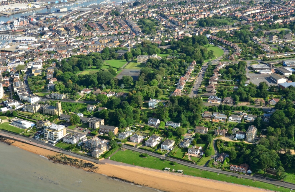 an aerial view of cowes seafront, showing green parks and the beach