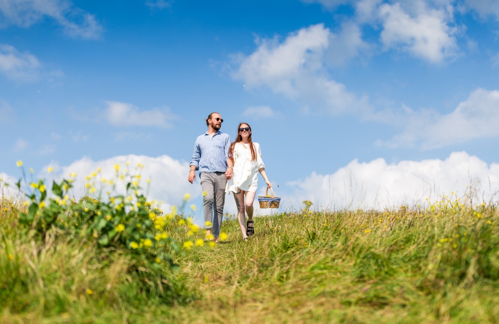 a smiling couple walking through the downs with a picnic basket