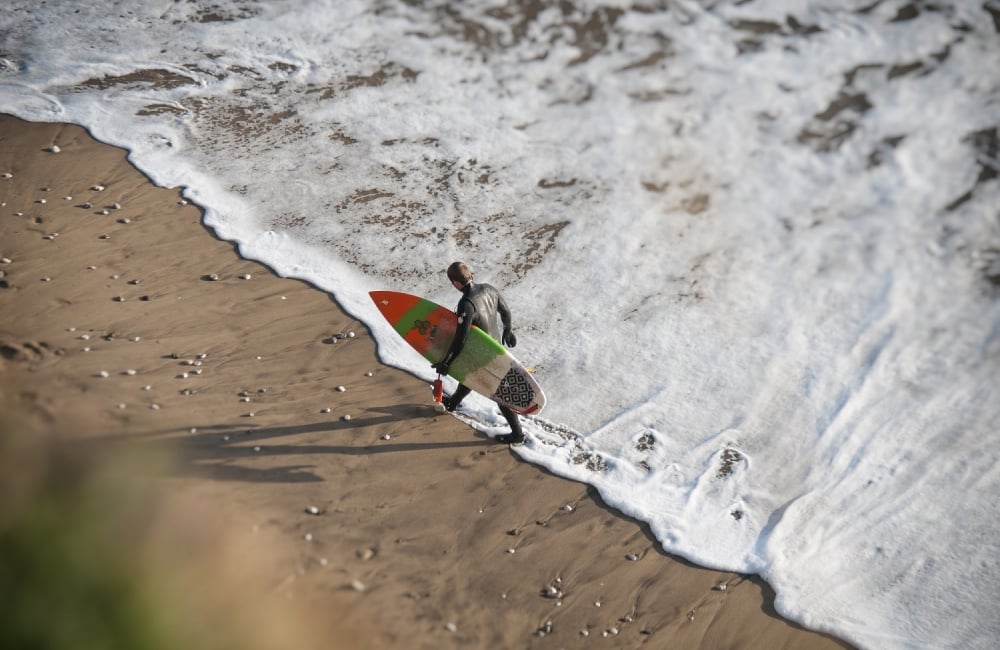 surfer walking across beach with board