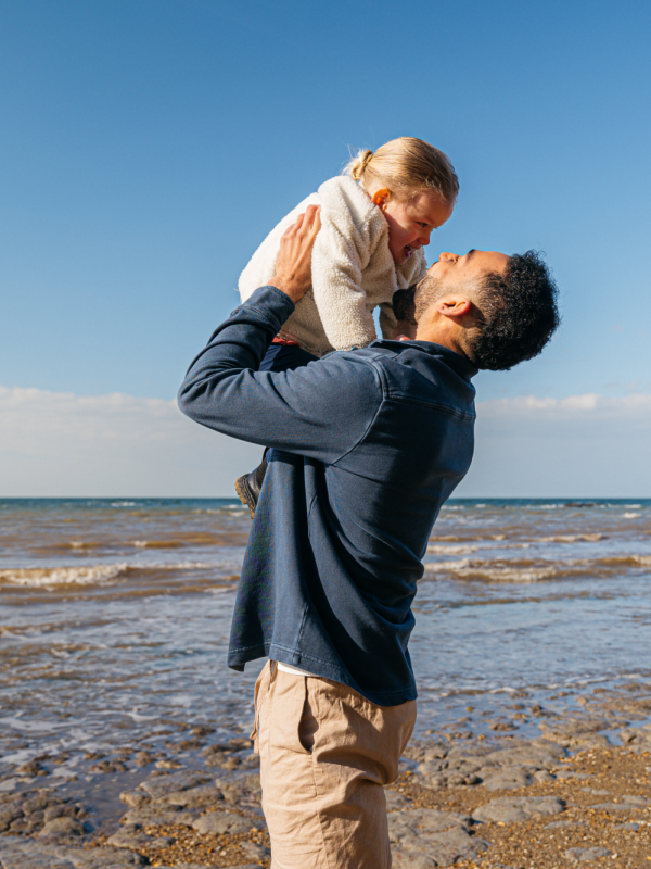 dad holds up young daughter on the beach