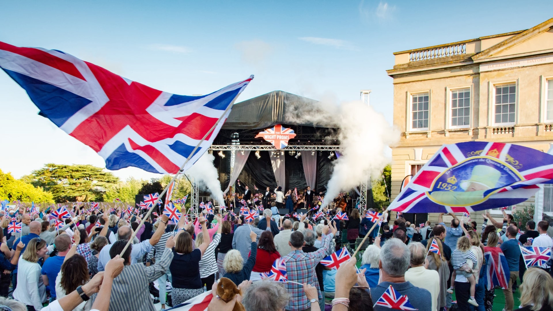 a crowd cheering and waving flags with the stage in the background