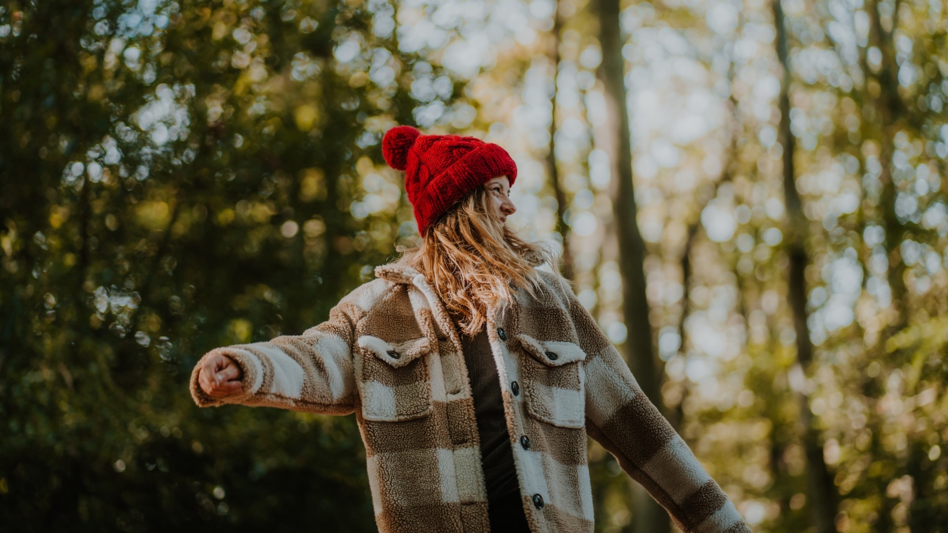 a girl with red bobble hat walking through woods