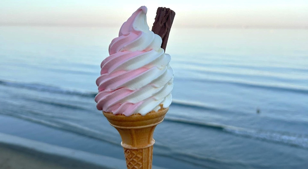 pink and white soft serve ice cream in a cone with chocolate flake