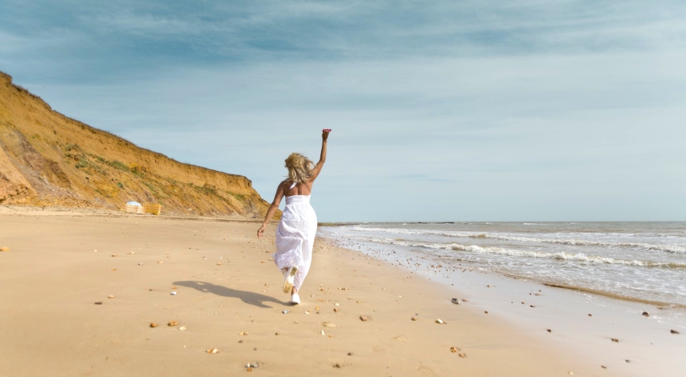 woman in white dress walks along the beach in summer