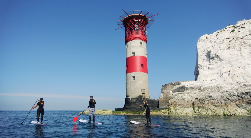 a group of people paddle boarding in front of the needles lighthouse