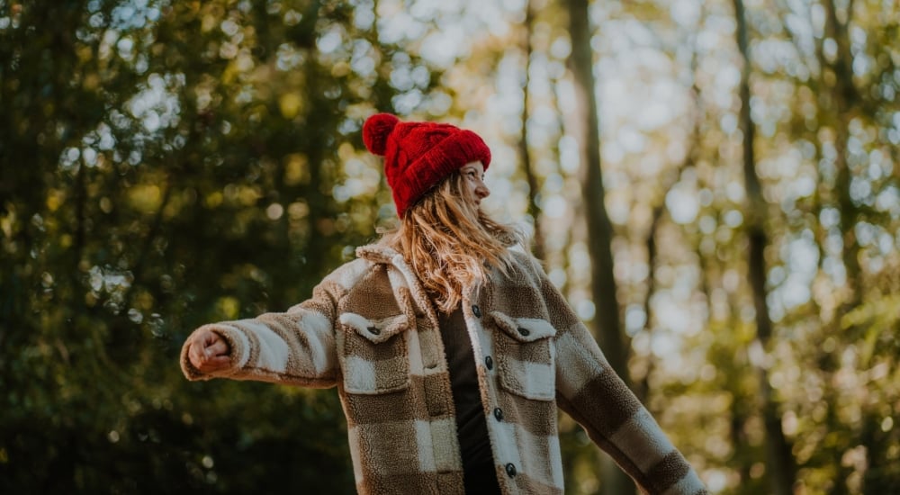 a girl with red bobble hat walking through woods