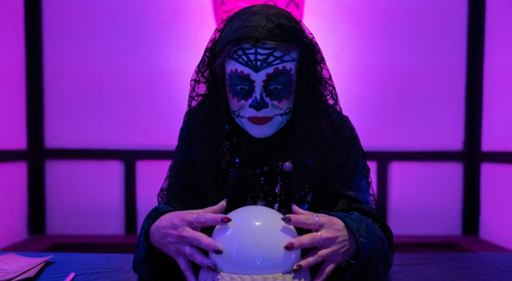 a fortune teller posing with crystal ball and sugar skull face paint