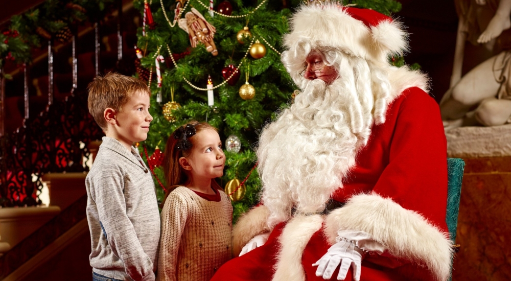 two children talking to father christmas in red suit and beard